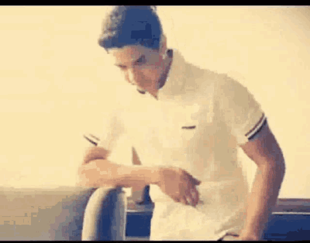 a man in a white shirt is standing next to a chair and taking off his shirt .