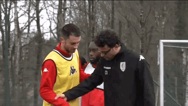 a man in a kappa jacket is helping another man walk