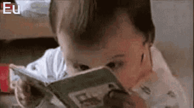 a baby is reading a book with his eyes closed while sitting on a bed .