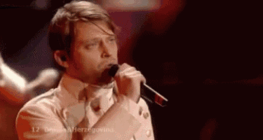 a man in a white shirt and tie is singing into a microphone .