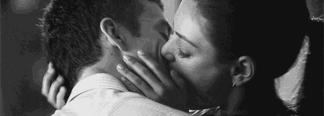 a black and white photo of a woman kissing a man on the neck .