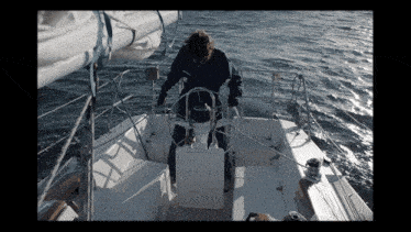 a man stands at the steering wheel of a sailboat in the ocean