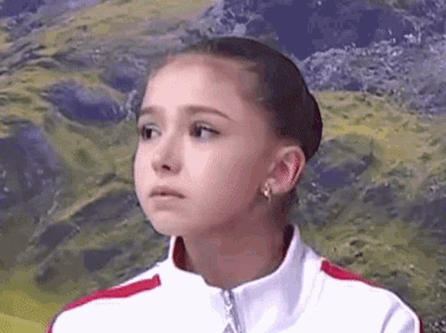 a young girl is wearing a white jacket with a red stripe and earrings .