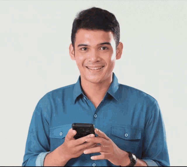 a man wearing a blue shirt is smiling while holding a cell phone