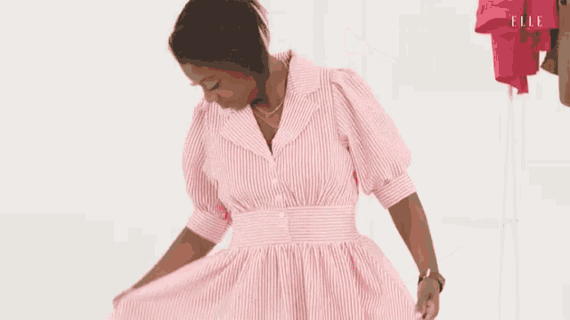 a woman is wearing a pink striped dress and standing in front of a white wall .