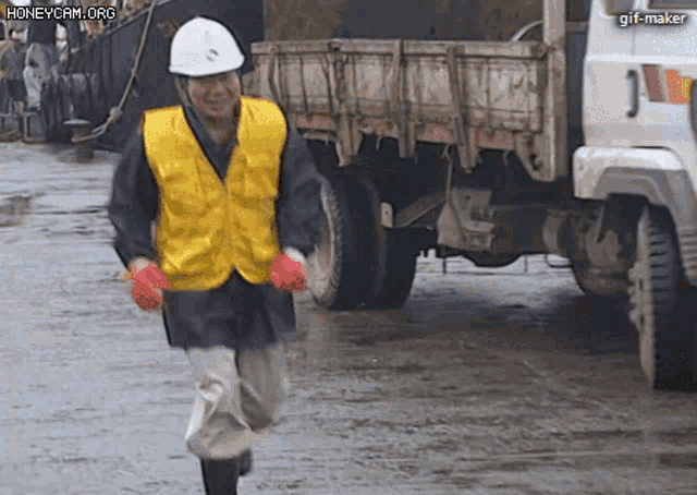 a man wearing a hard hat and a yellow vest is running in front of a truck that says j on the back