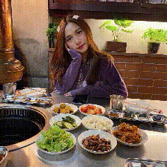 a woman in a purple sweater sits at a table with bowls of food on it