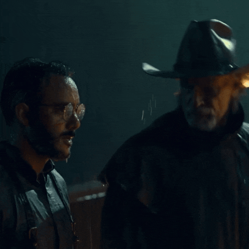 a man in a cowboy hat is holding another man 's hand in the rain