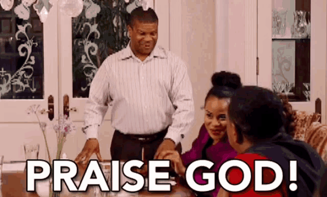 a man is standing in front of a table with a group of people sitting at it and saying praise god .