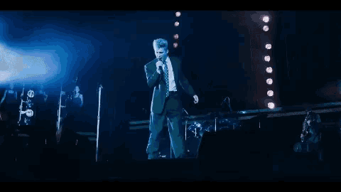a man in a suit is singing into a microphone on a stage .