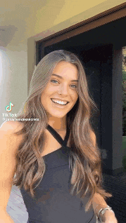 a woman with long brown hair is smiling and wearing a black tank top .