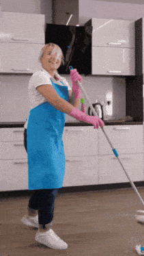 a woman in a blue apron and pink gloves mopping the floor