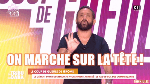 a man with a beard stands in front of a sign that says on marche sur la tete !