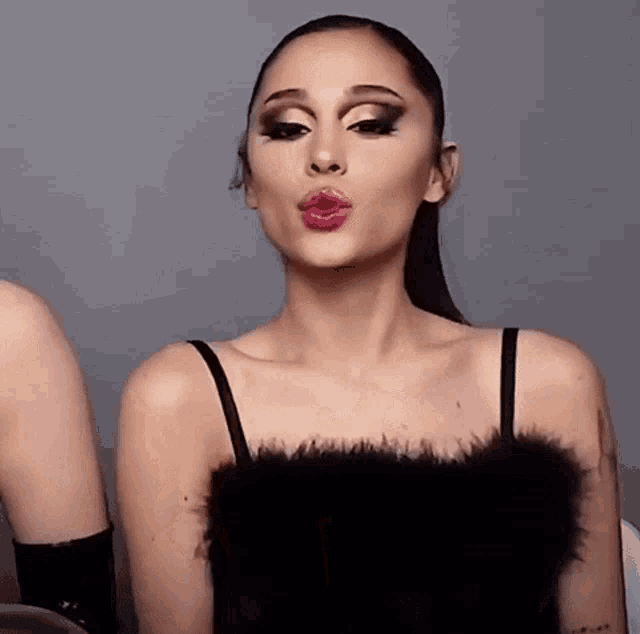 ariana grande is wearing a black feathered top and making a face .