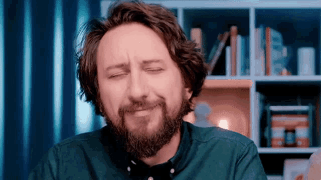 a man with a beard is making a funny face while sitting in front of a bookshelf .