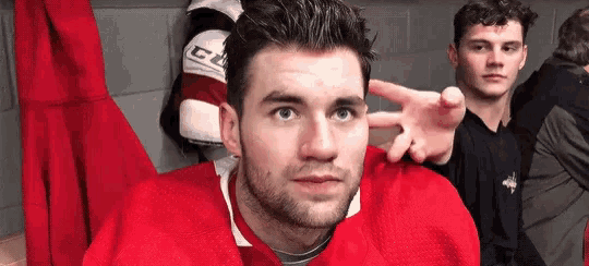 a man in a red hockey jersey is sitting in a locker room with his hands on his head .