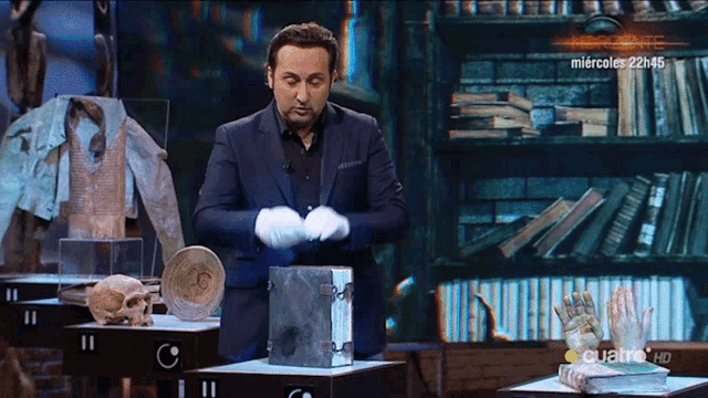 a man in a suit and white gloves stands in front of a bookshelf with a sign that says miércoles 22h 45