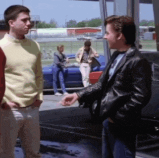 a man in a black leather jacket is talking to another man in a yellow sweater