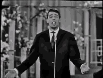 a man in a suit and tie is singing into a microphone on a stage .