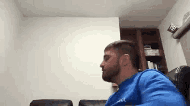 a man with a beard is sitting on a couch in a living room with his mouth open .