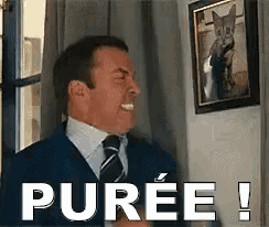 a man in a suit and tie is standing in front of a picture that says puree