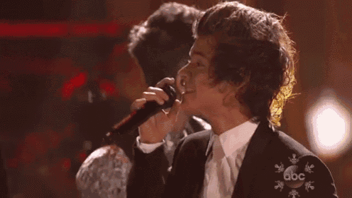 a man in a suit is singing into a microphone while another man stands behind him .