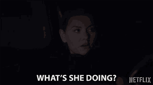 a woman in a dark room is asking what 's she doing ?