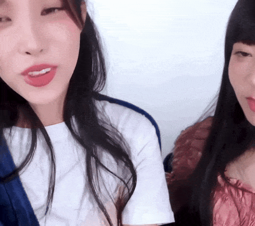 two women are looking at the camera with one wearing a white shirt and the other wearing a pink top
