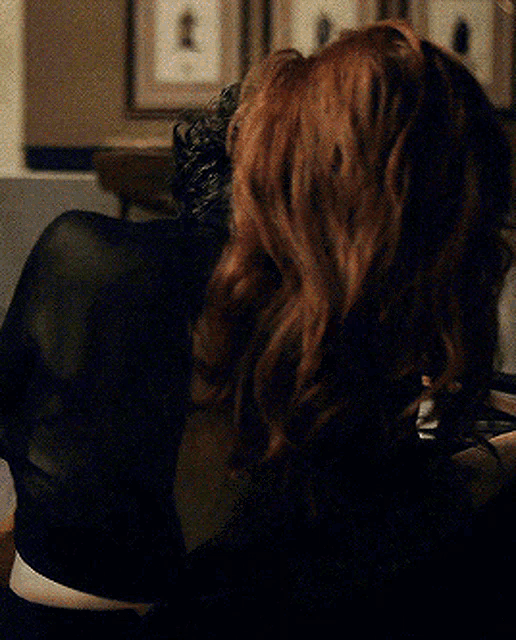 a woman with red hair is sitting in a chair with her back to the camera