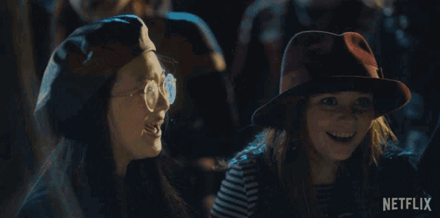 two girls wearing hats and glasses are laughing in front of a netflix logo