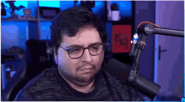 a man wearing glasses and headphones is sitting in front of a blue microphone .