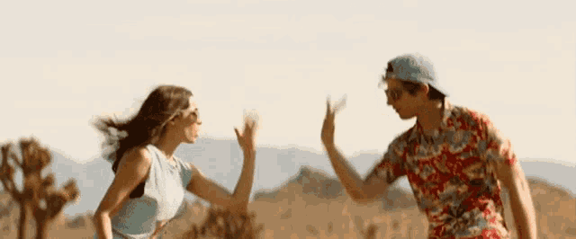 a man and a woman are giving each other a high five while standing in the desert .