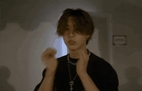 a young man wearing a black shirt and a chain around his neck giving the middle finger