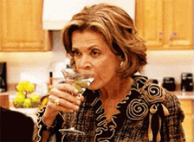 a woman is drinking from a martini glass in a kitchen