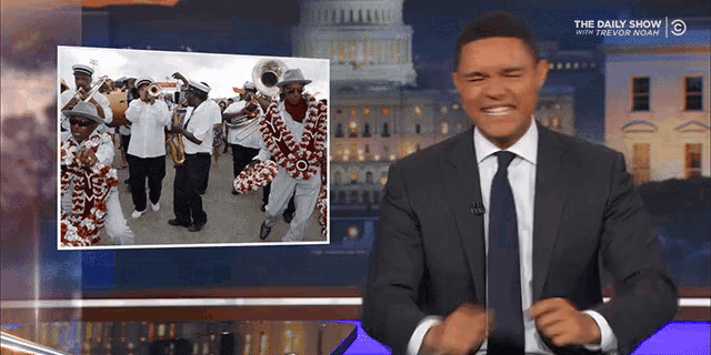 a man in a suit and tie is standing in front of a picture of a band on the daily show
