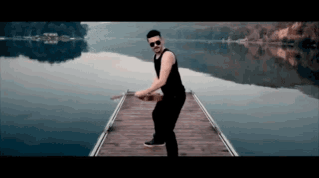 a man is standing on a dock near a lake holding a guitar