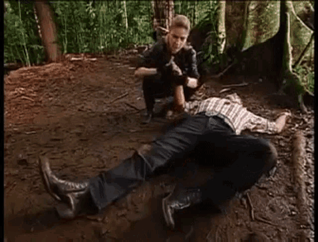 a man is laying on the ground in the woods while a woman looks on .