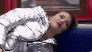 a woman wearing a silver jacket is laying on a blue couch .