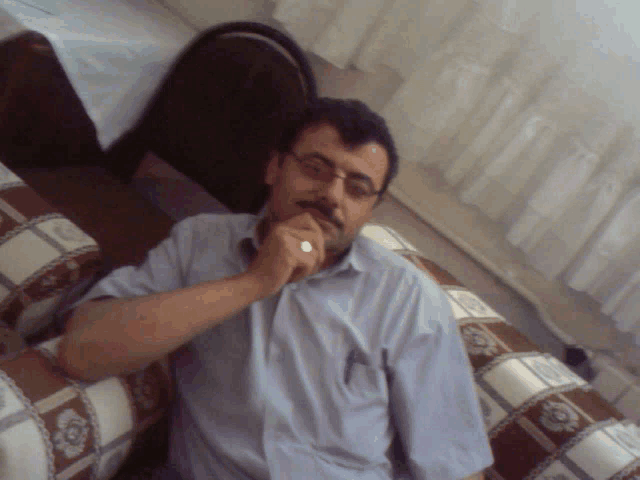 a man wearing glasses and a watch sits on a couch with his hand on his chin