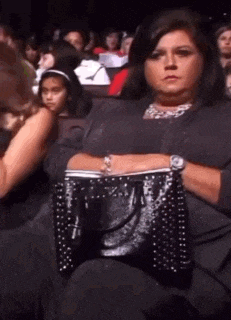 a woman is sitting in a theater holding a black purse and a watch .