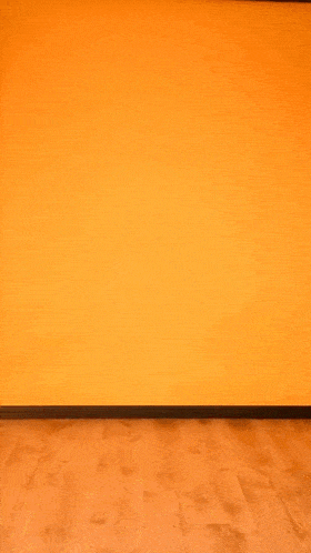 a woman in a black dress is dancing against an orange wall