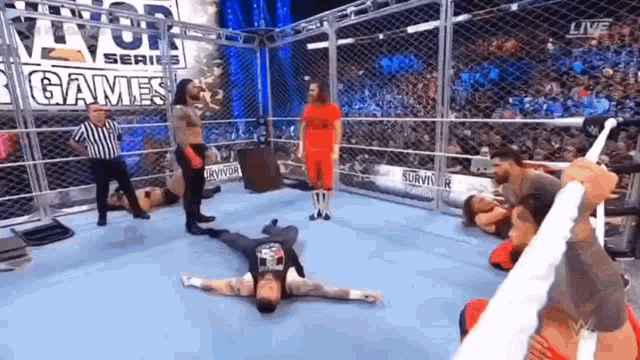 a group of wrestlers are laying on the ground in a wrestling ring while a referee watches .