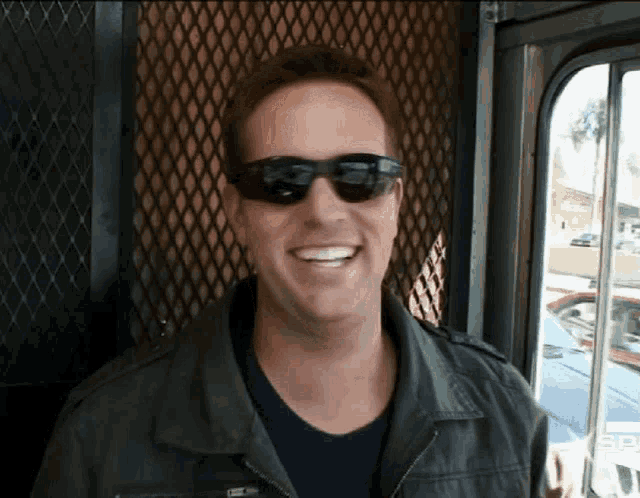 a man wearing sunglasses and a black jacket smiles for the camera