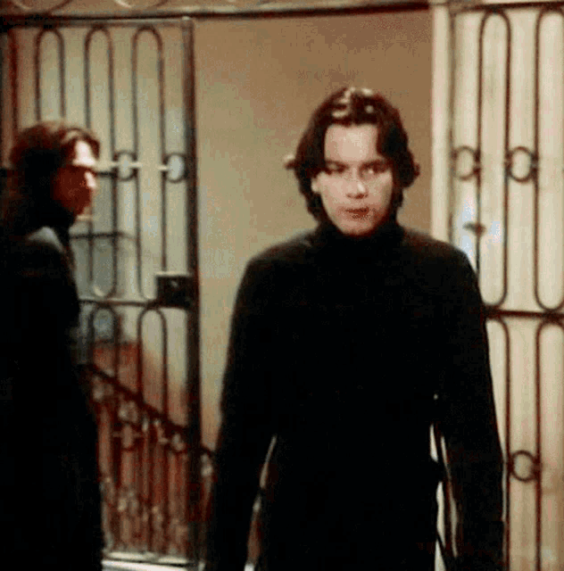a man in a black turtleneck is standing in front of a gate