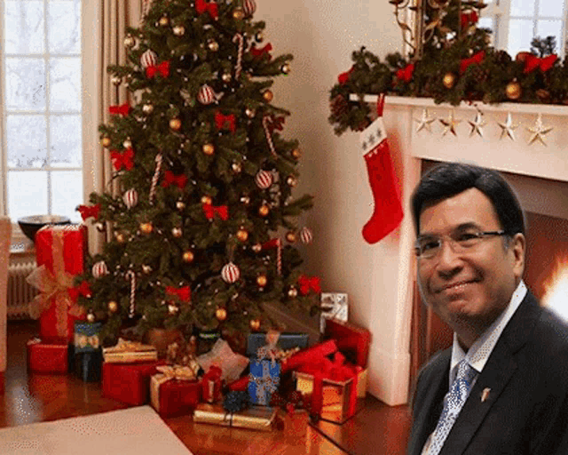 a man in a suit and tie is smiling in front of a christmas tree and fireplace