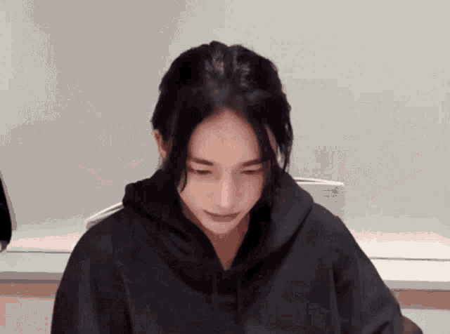 a young woman wearing a black hoodie is sitting at a table .