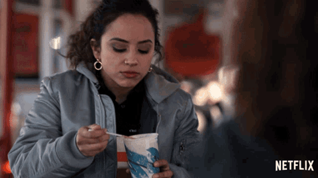 a woman in a grey jacket is eating ice cream with a spoon from a netflix advertisement