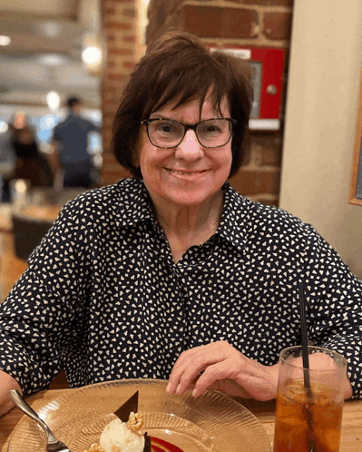 a woman in glasses sits at a table with a plate of food