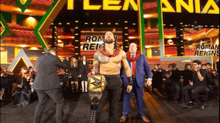 a man in a suit is holding a wrestling championship belt while standing in front of a crowd .