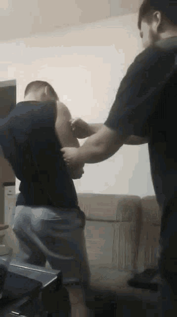 two men are standing next to each other in a living room and one of them is holding the other 's arm .